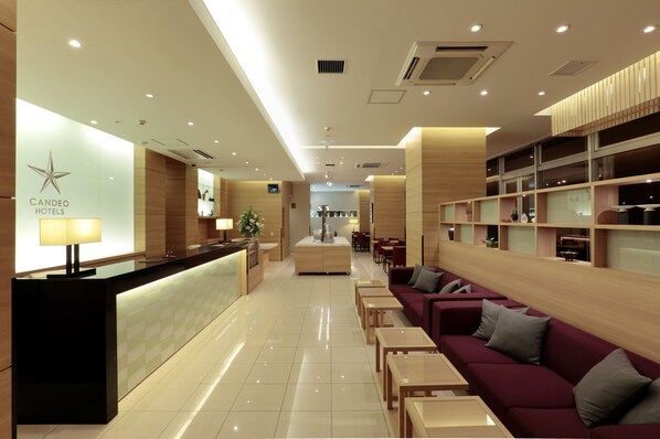 Un hall de hotel con una recepción, una zona de estar y una escalera que sube al piso superior.
