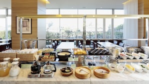 A buffet setup with various food items and condiments, a coffee machine, and a view of the outdoors through large windows.