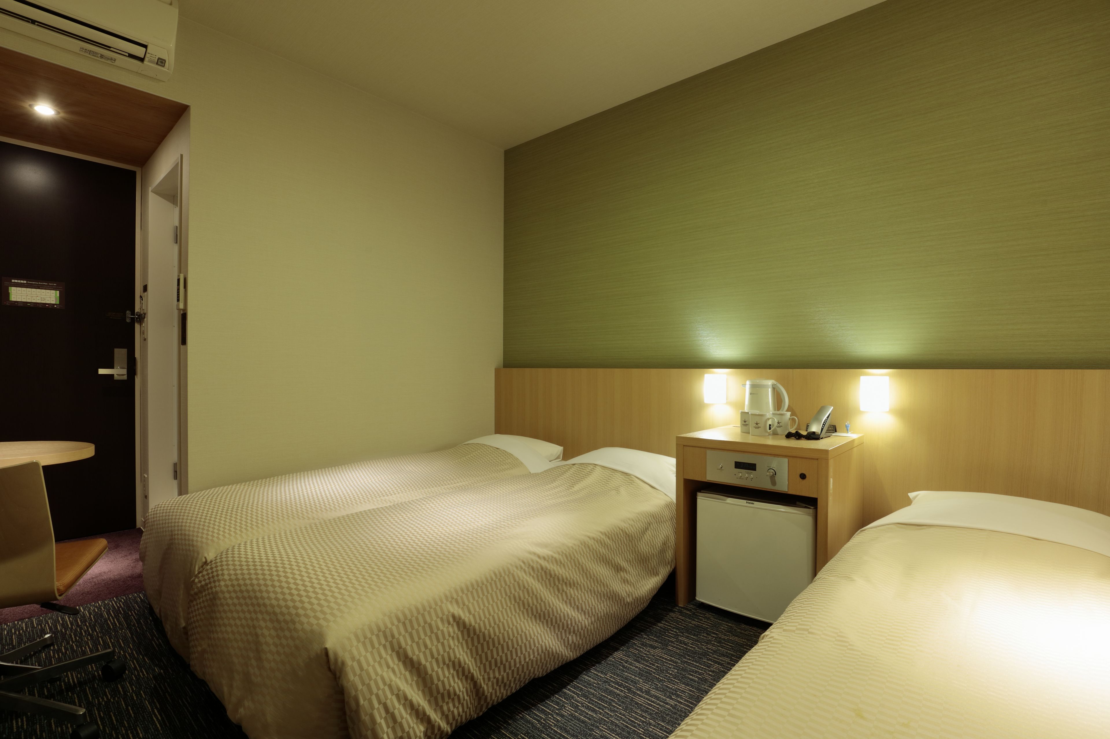 A hotel room with two beds, a small desk with a coffee maker, and a mini fridge.