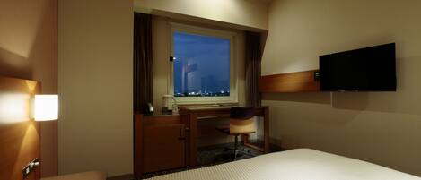 Habitación de hotel con cama, escritorio, silla, televisión y ventana con vista a la ciudad.
