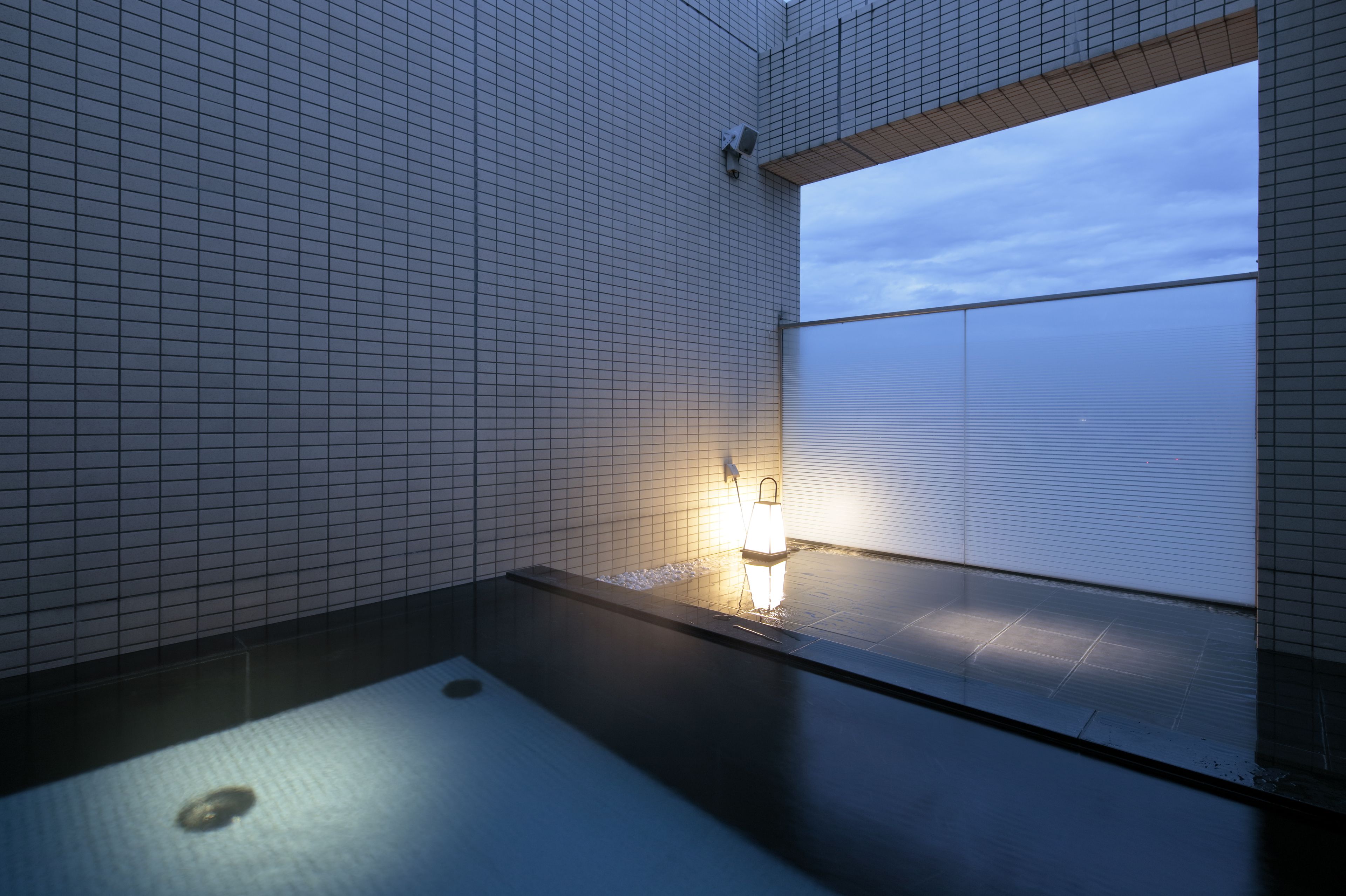 Un baño moderno con suelo de baldosas, un lavamanos pequeño y una ventana con persianas.