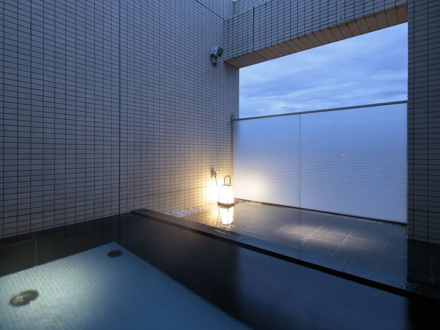 Un baño moderno con suelo de baldosas, un lavamanos pequeño y una ventana con persianas.