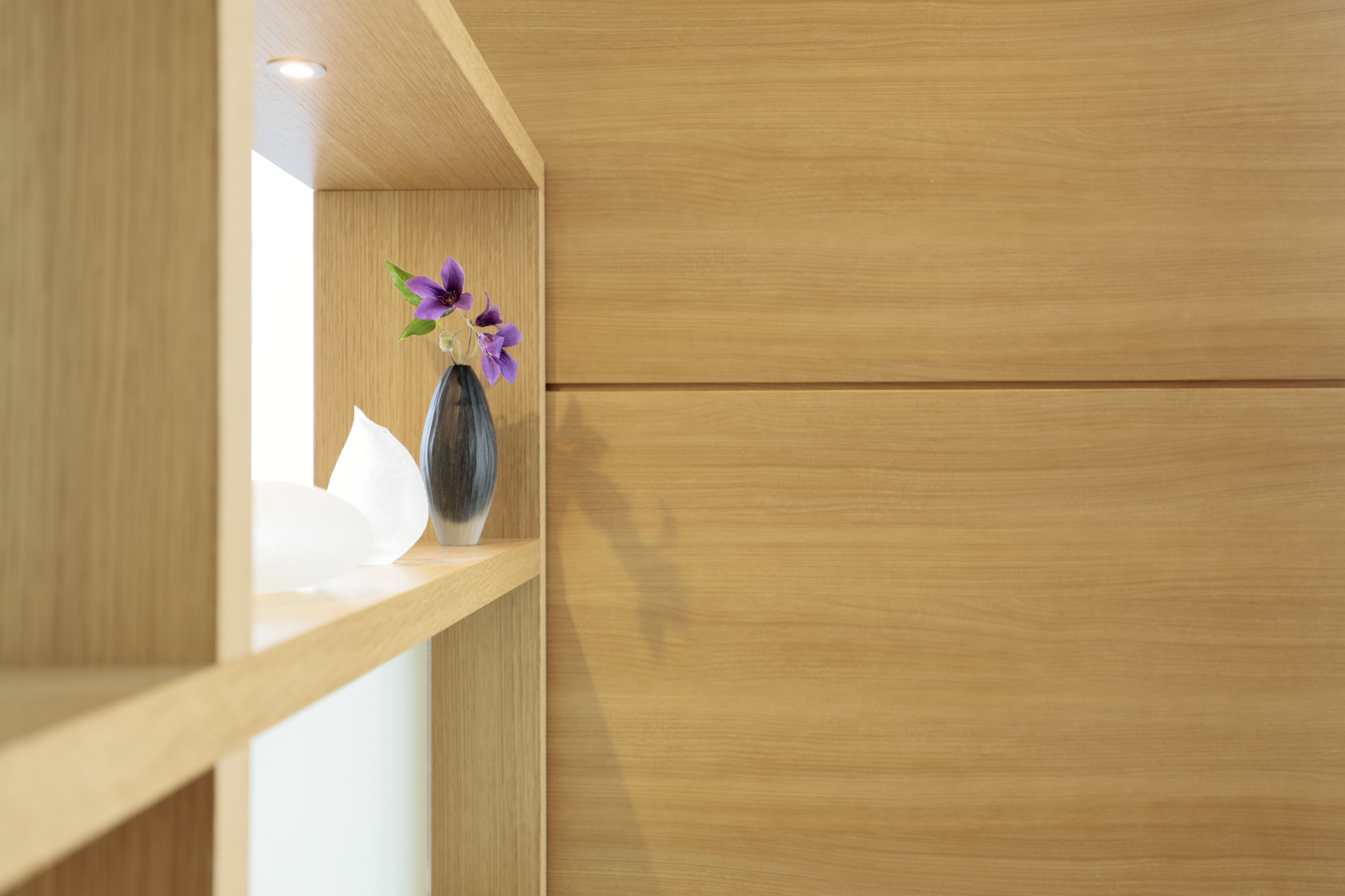 Une étagère en bois sur laquelle est posé un vase rempli de fleurs violettes.