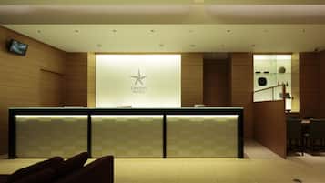A hotel reception area with a modern design, featuring a reception desk, a digital screen, and a glass display case.