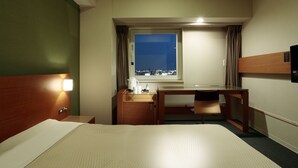 Ett hotellrum med en säng, ett skrivbord, en stol, ett fönster med utsikt över staden och ett nattduksbord.