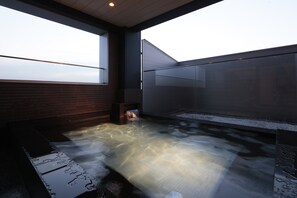 Zona de hidromasaje con vista al cielo a través de un ventanal grande, un banco de madera y suelo de baldosas.