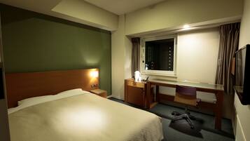 Habitación de hotel con cama, escritorio, silla, mesita de noche, lámpara y ventana con cortinas.