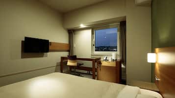 A hotel room with a bed, a desk, a chair, a TV, a window with a night view, and a bedside table.