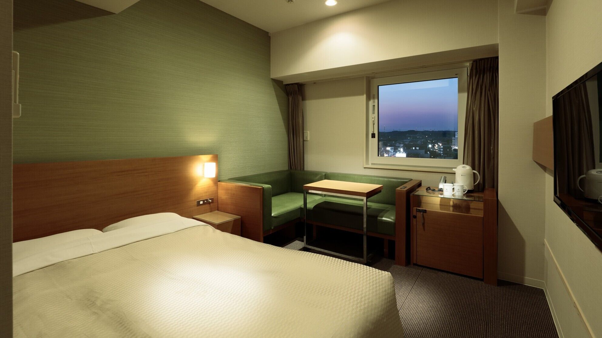 Ein Hotelzimmer mit Bett, Schreibtisch, Stuhl, Fenster mit Stadtblick und Fernseher.