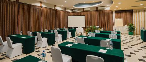 Un salón de conferencias con varias mesas, sillas y una pantalla grande.