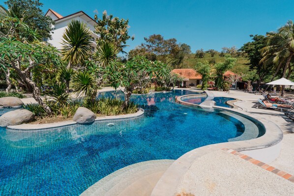 Una piscina de diseño curvo, rodeada de rocas y plantas tropicales.
