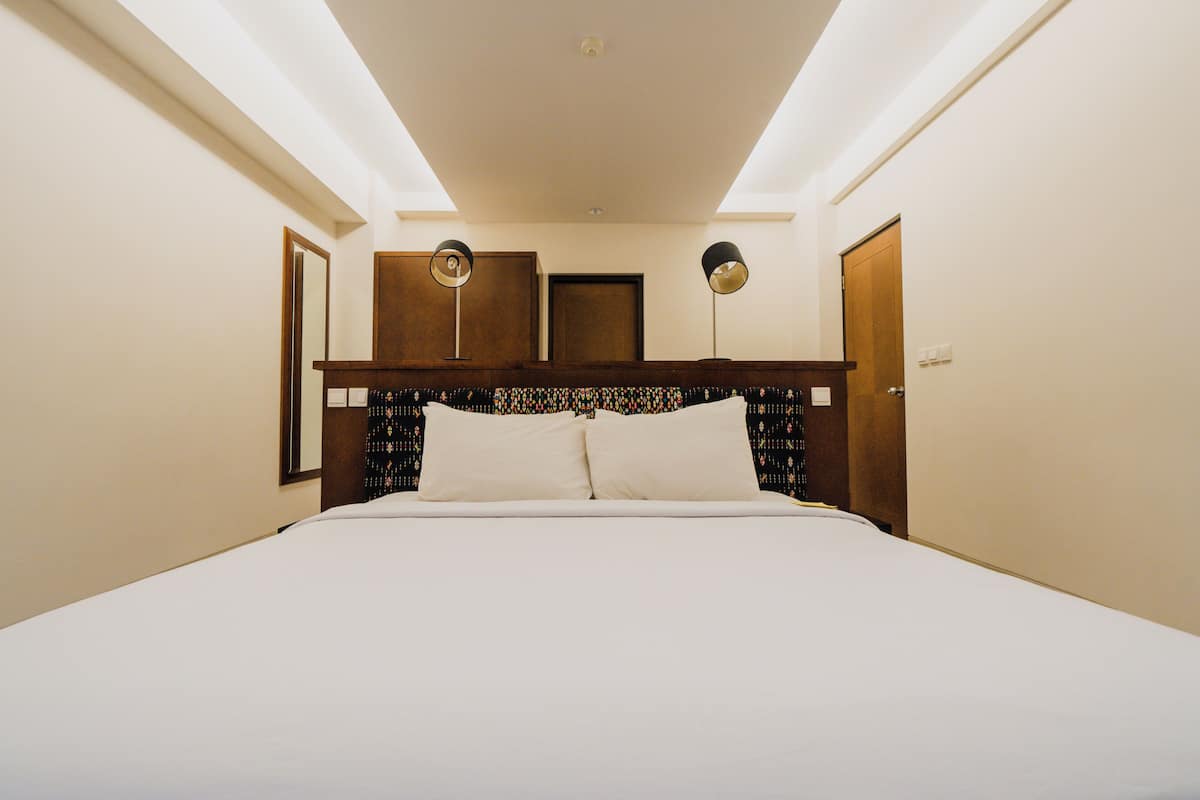 Quarto de hotel com uma cama grande, duas luminárias de cabeceira, um painel de madeira na cabeceira e um espelho.