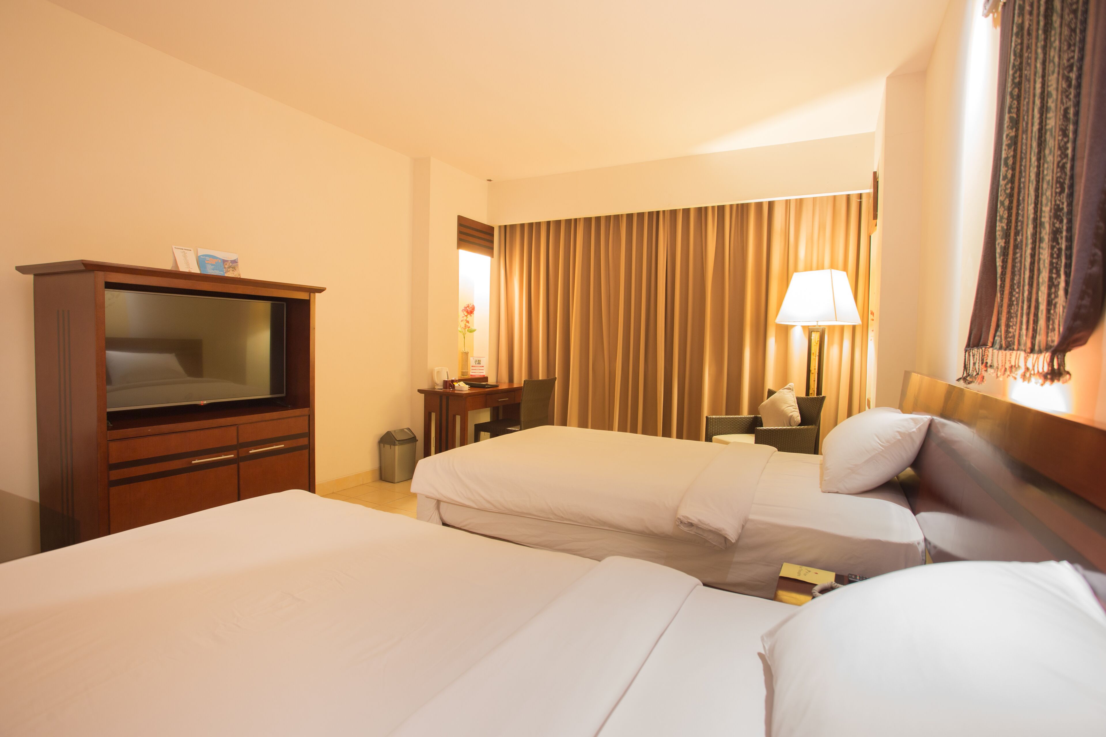 Ein Hotelzimmer mit zwei Betten, einem Schreibtisch, einem Fernseher und einer Lampe.