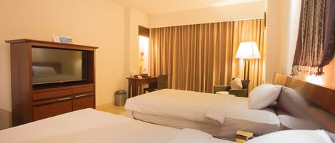A hotel room with two beds, a desk, a television, and a lamp.