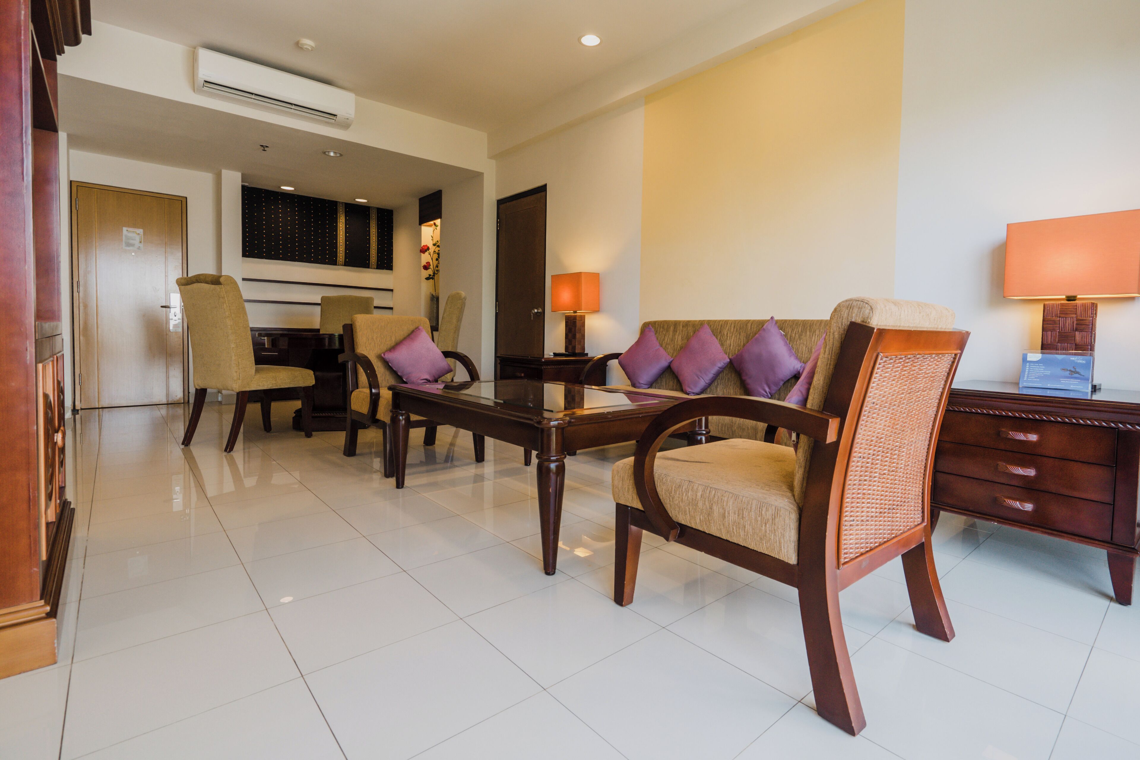 A hotel room with a dining table, chairs, a sofa, a lamp, and a wooden cabinet.