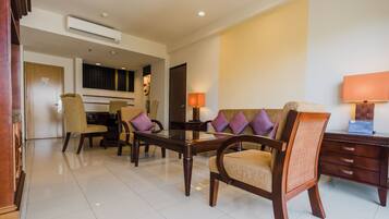 A hotel room with a dining table, chairs, a sofa, a lamp, and a wooden cabinet.