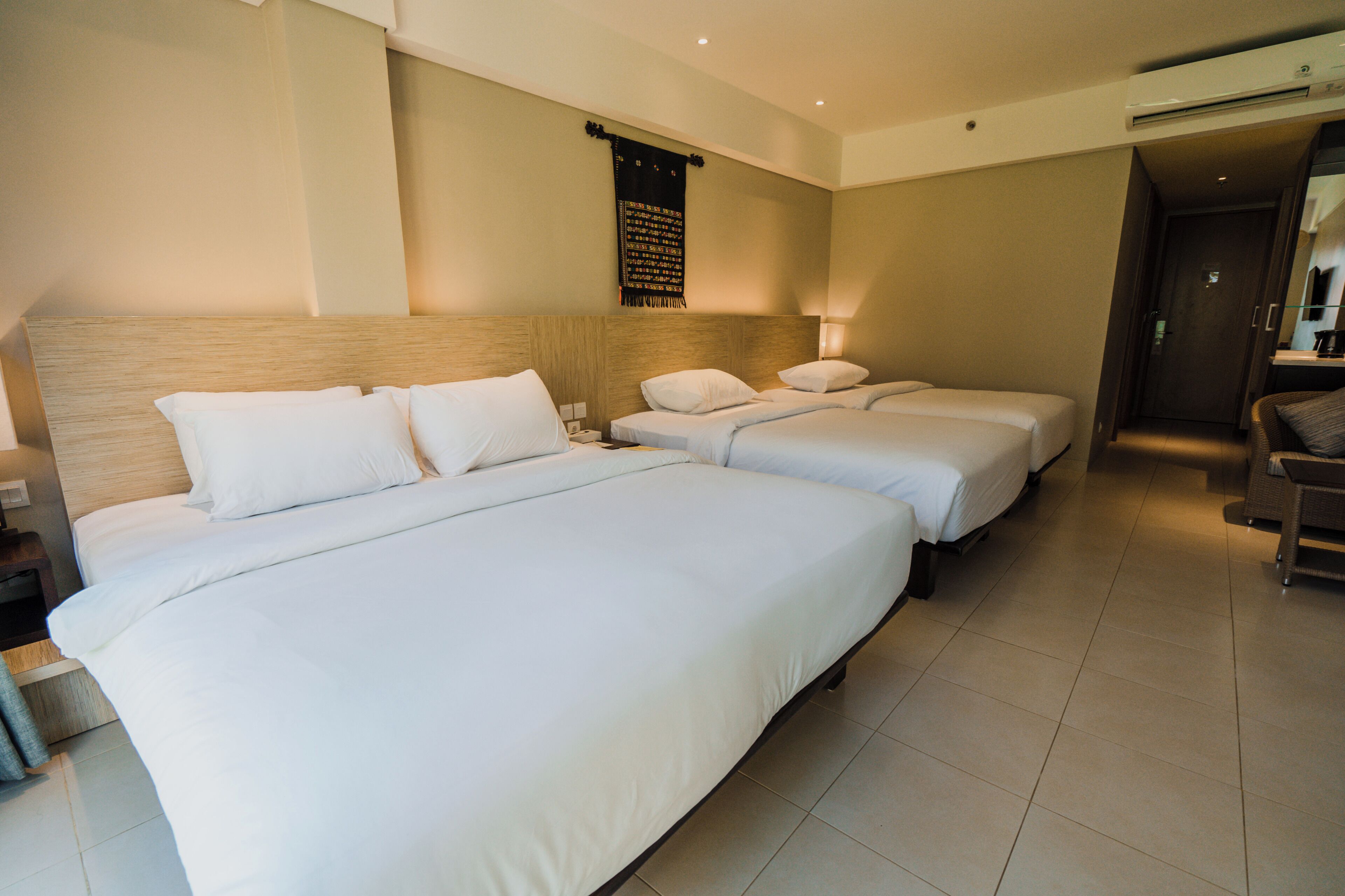 A hotel room with two beds, a headboard, a wall-mounted tapestry, and a small seating area with a table and chairs.