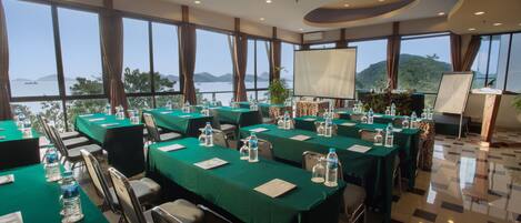 A conference room with multiple tables, chairs, and a large screen.
