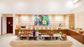 Um lobby de hotel moderno com um balcão de recepção central, uma grande pintura abstrata e diversos serviços, como plantas e expositores de comida.