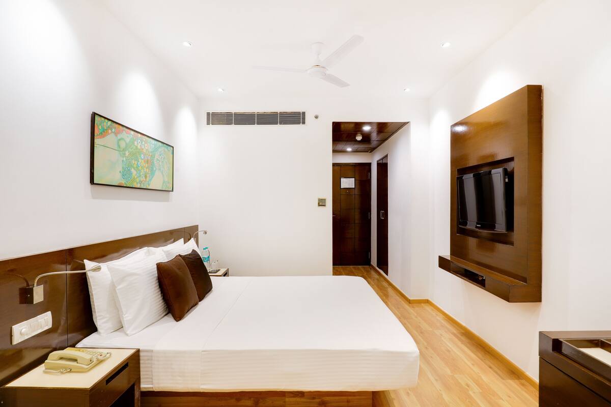 Ein modernes Hotelzimmer mit einem großen Bett, einem Wand-Fernseher, einem Deckenventilator und einem Gemälde an der Wand.