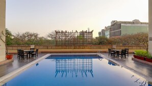 Piscina no terraço com vista desobstruída da paisagem urbana, rodeada por móveis de exterior e plantas em vasos.
