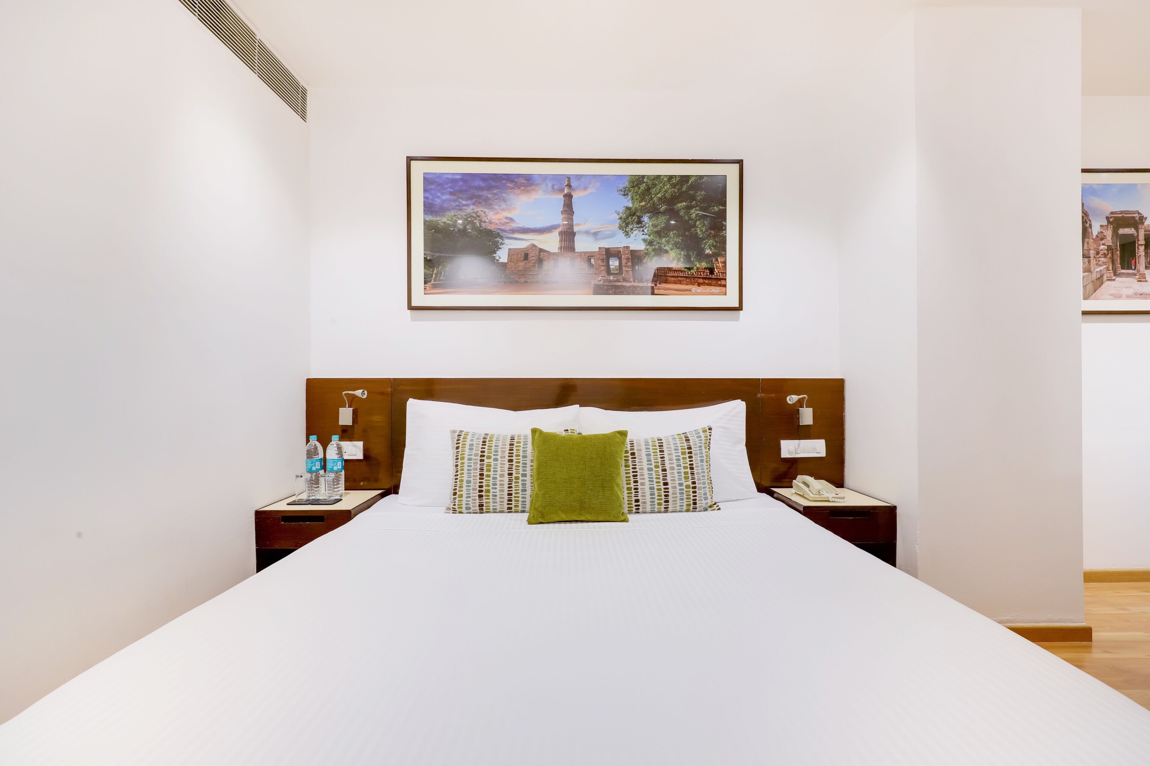 A hotel room with a large bed, a wooden headboard, two bedside tables with lamps, and a framed picture on the wall.