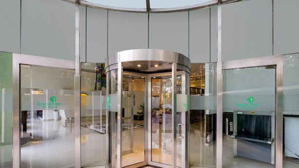 Uma porta giratória com painéis de vidro e estrutura metálica, dando acesso a um edifício com fachada de vidro.