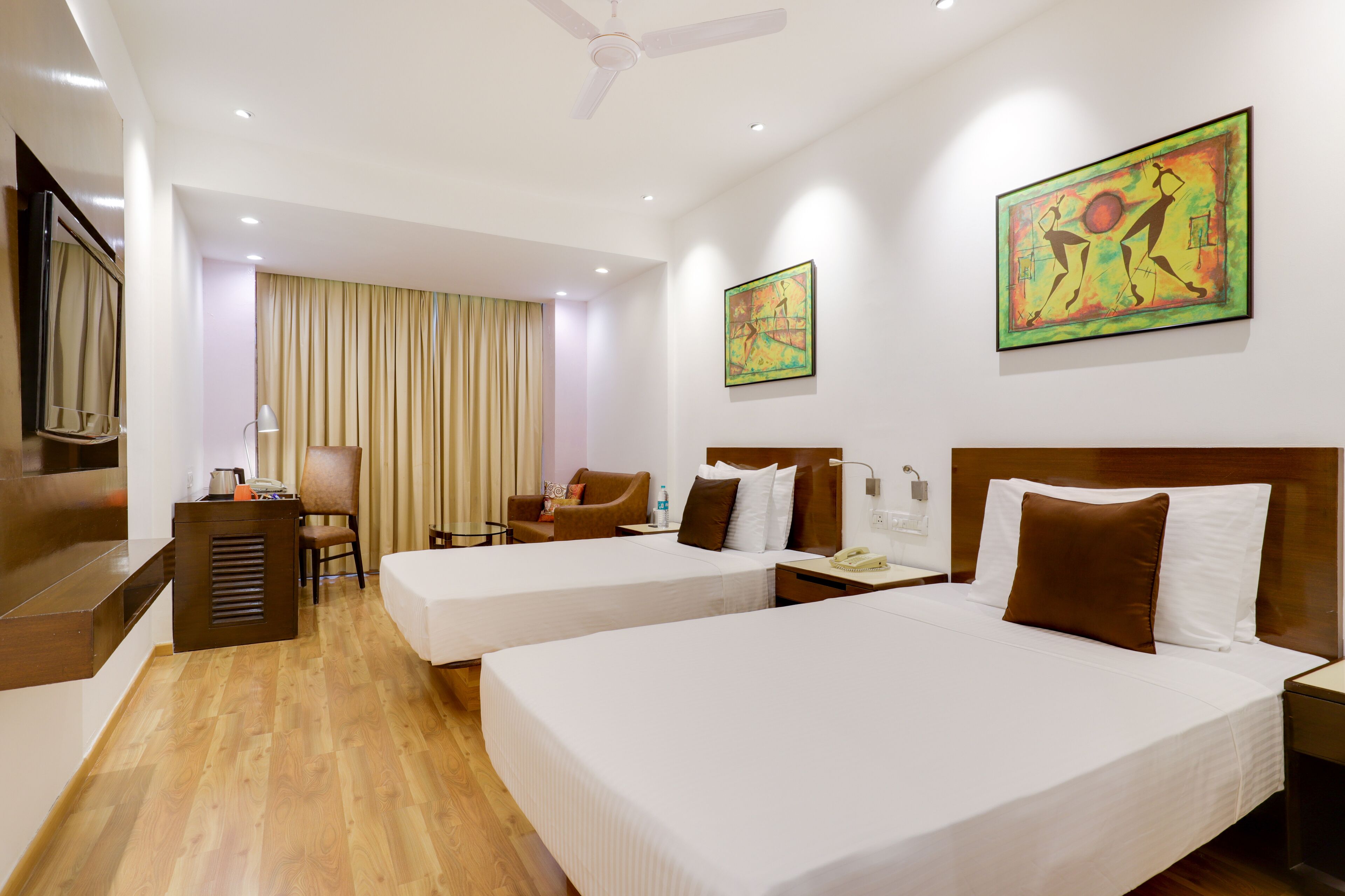 A hotel room with two beds, a desk, a chair, and artwork on the walls.