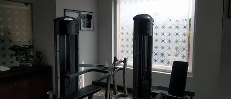 Ein Heimfitnessraum mit Trainingsgeräten, einem Fenster mit Milchglas und einer Wanddekoration.