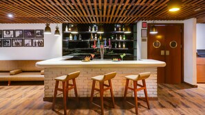 Uma área de bar com teto de madeira, banquetas e um balcão com garrafas e copos.