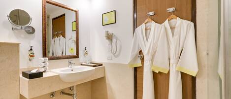 A bathroom with a sink, mirror, and two white robes hanging on a wooden door.