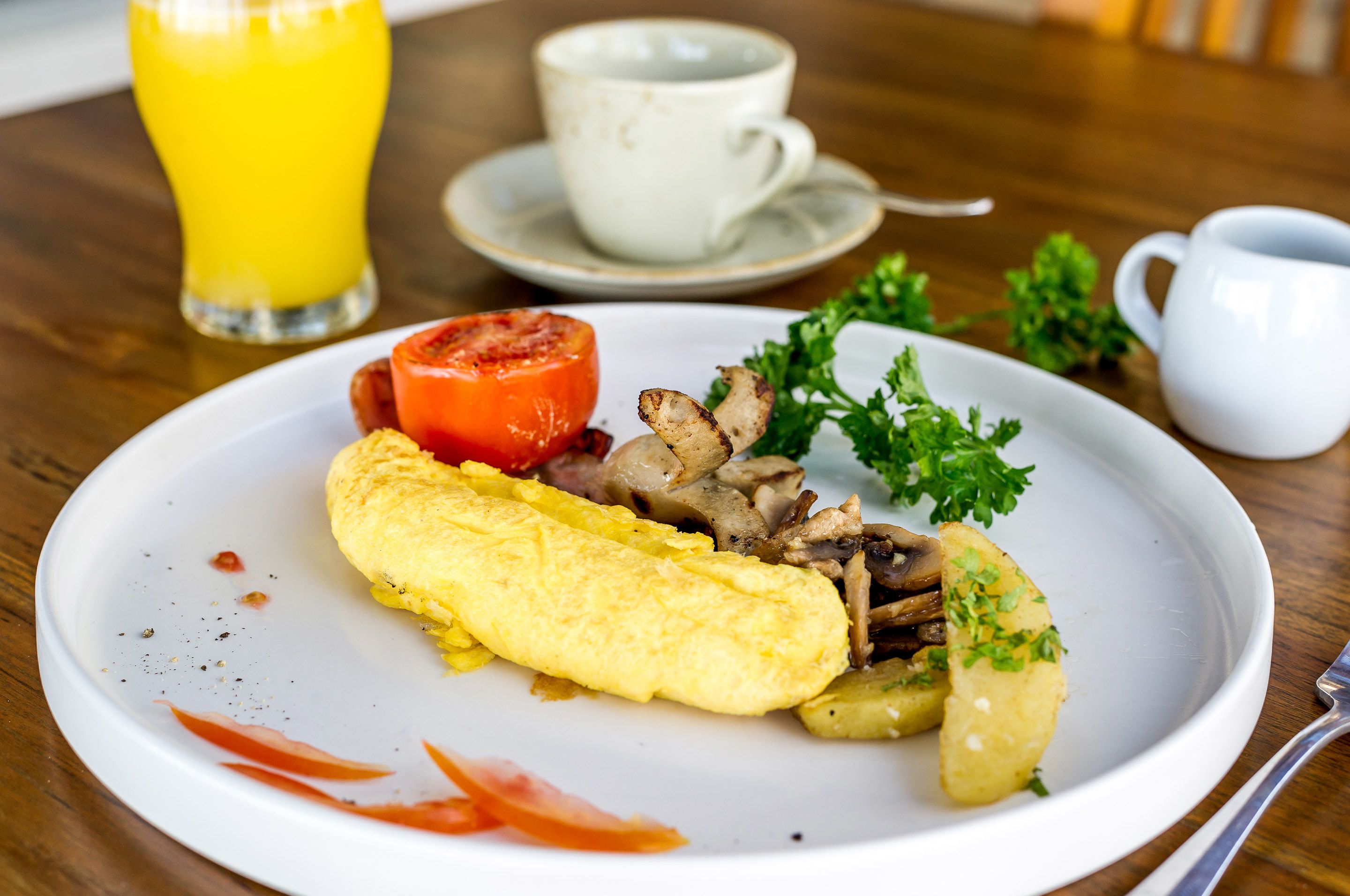 Un piatto con un'omelette, pomodoro, funghi e prezzemolo su un tavolo di legno.