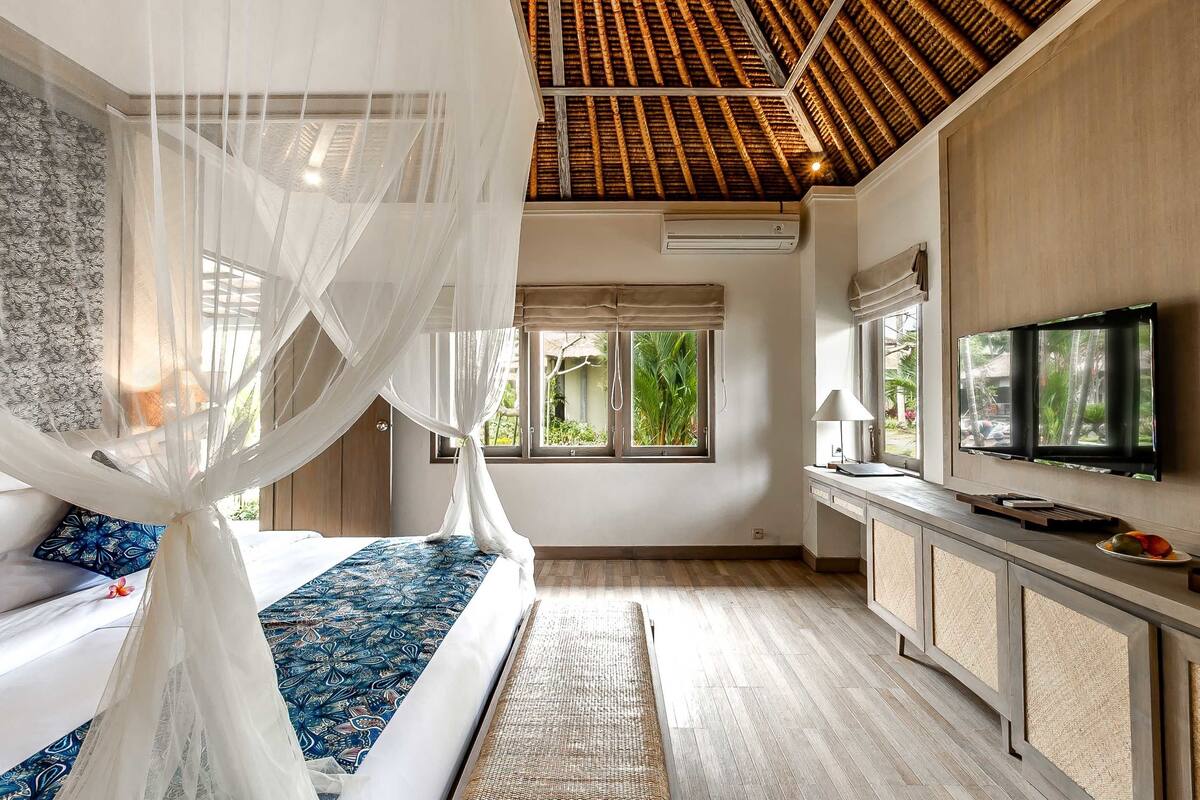 A bedroom with a bed, a TV, a window, and a ceiling fan.