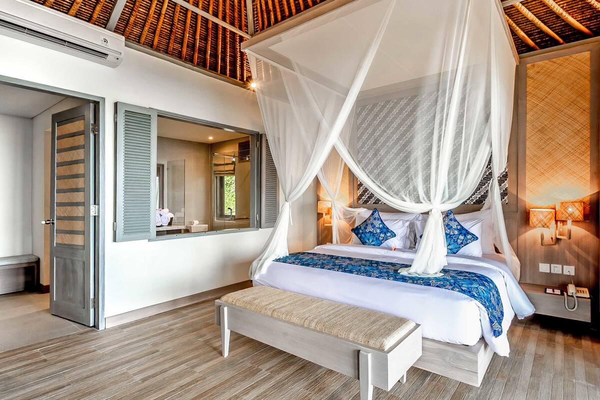 A bedroom with a canopy bed, a bench, a bedside table, and a mirror.