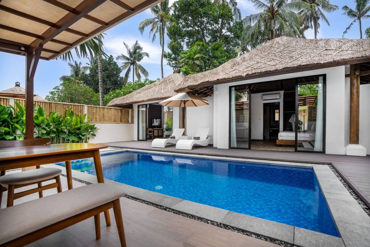 A modern pool area with a clear blue pool, lounge chairs, and a covered seating area with a thatched roof.