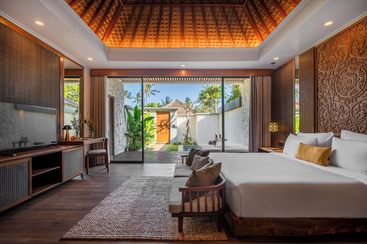 A spacious bedroom with a large bed, a TV, and a seating area with a view of the garden.
