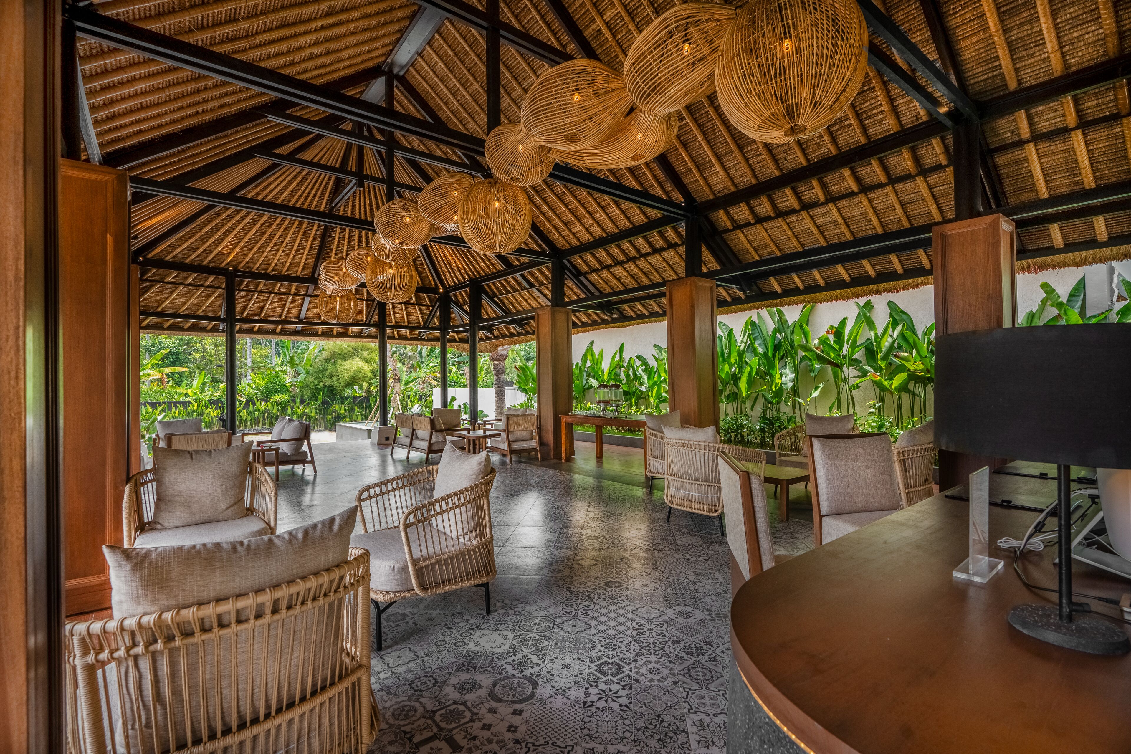 An open-air lounge with wicker furniture, a patterned floor, and a thatched roof.