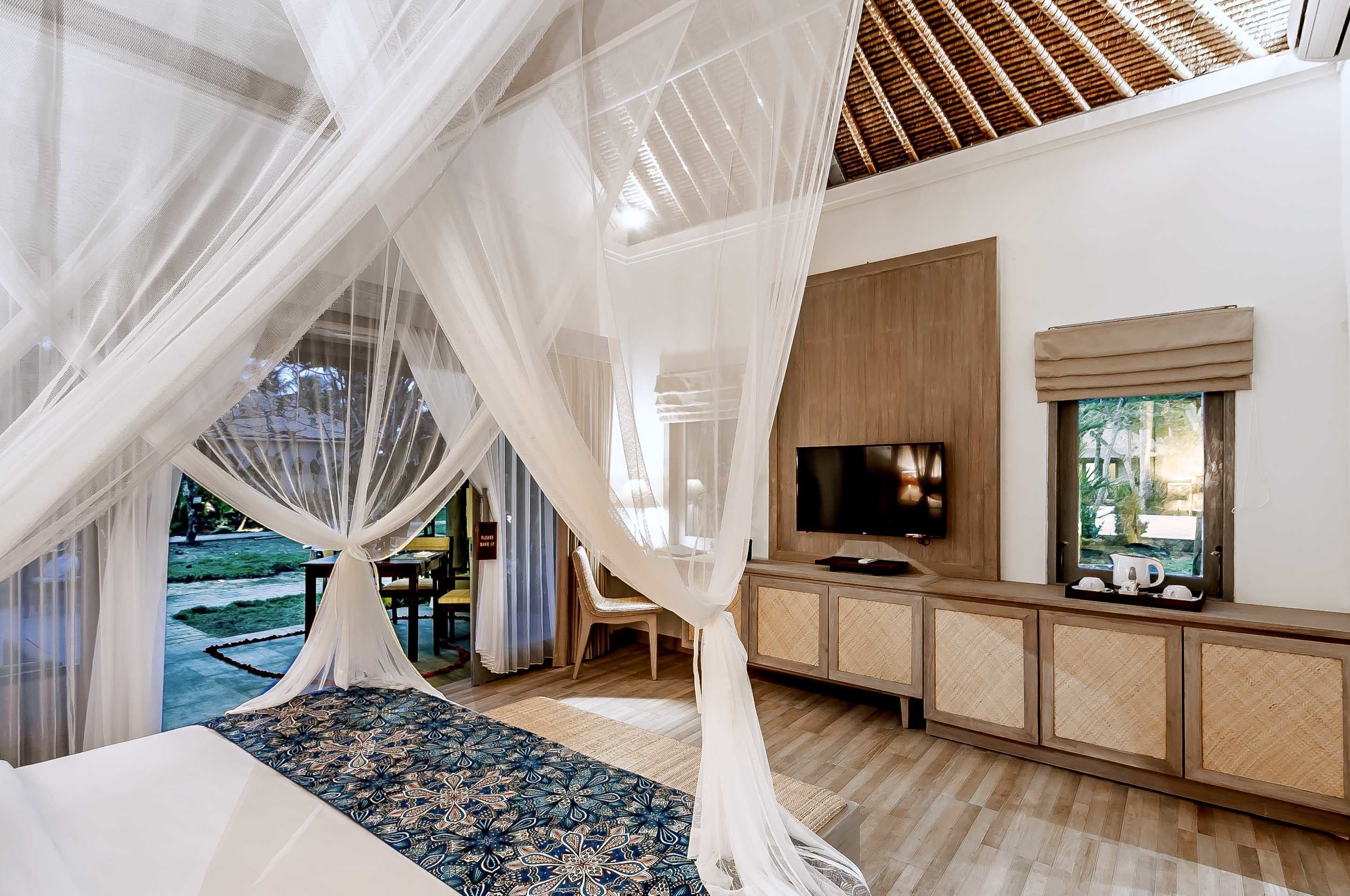 A bedroom with a bed, a TV, and a view of a garden.