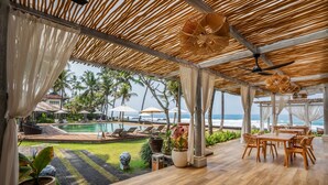 A covered outdoor area with a pool, lounge chairs, and a dining table. - Nirwana Beach & Resort (Manggis)