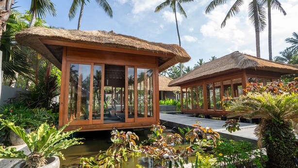 A resort with thatched-roof structures, a water feature, and tropical vegetation. - Nirwana Beach & Resort (Manggis)