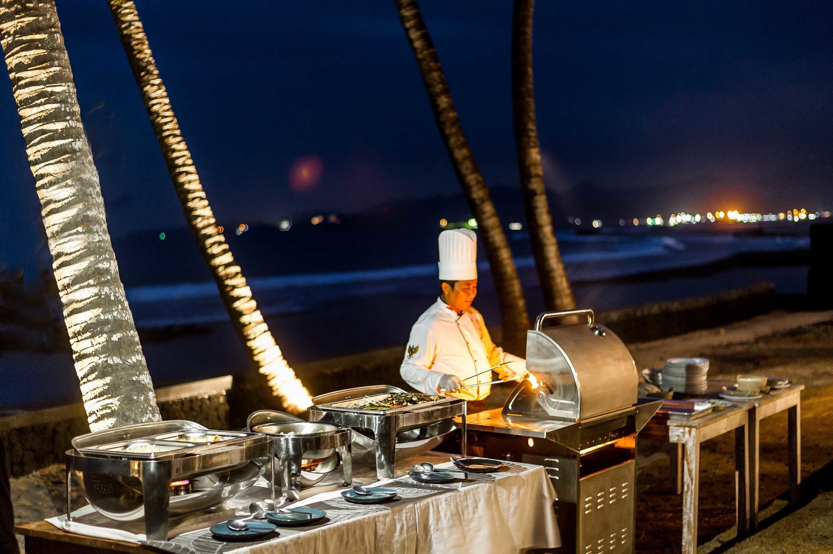 Un chef preparando comida al aire libre por la noche, con una parrilla y un bufé.