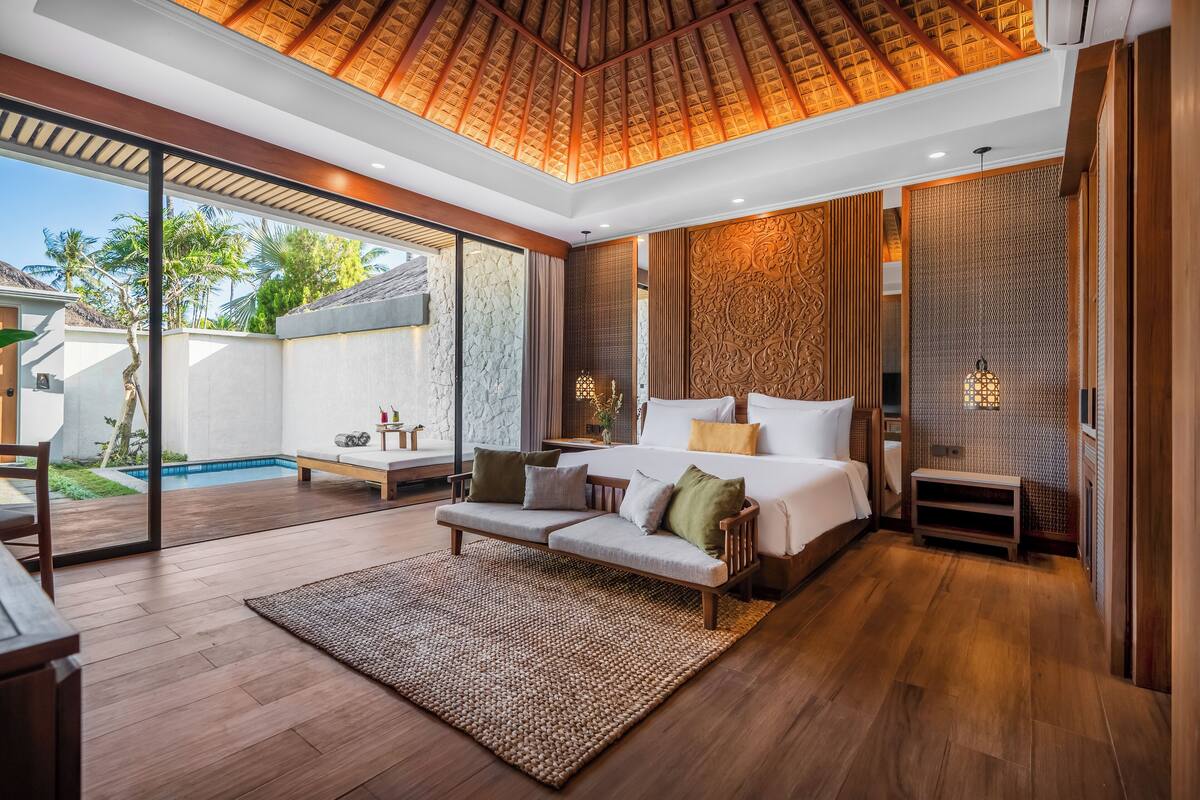 A modern bedroom with a large bed, a sofa, and a view of a swimming pool.