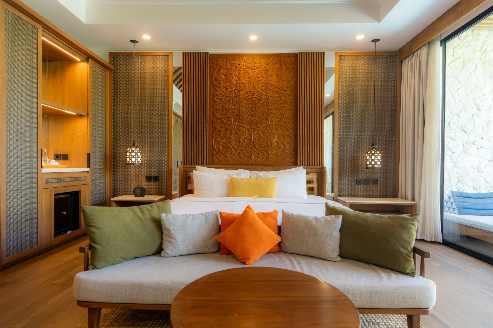 Quarto de hotel com cama, sofá, mesa de centro de madeira e vista para o exterior.