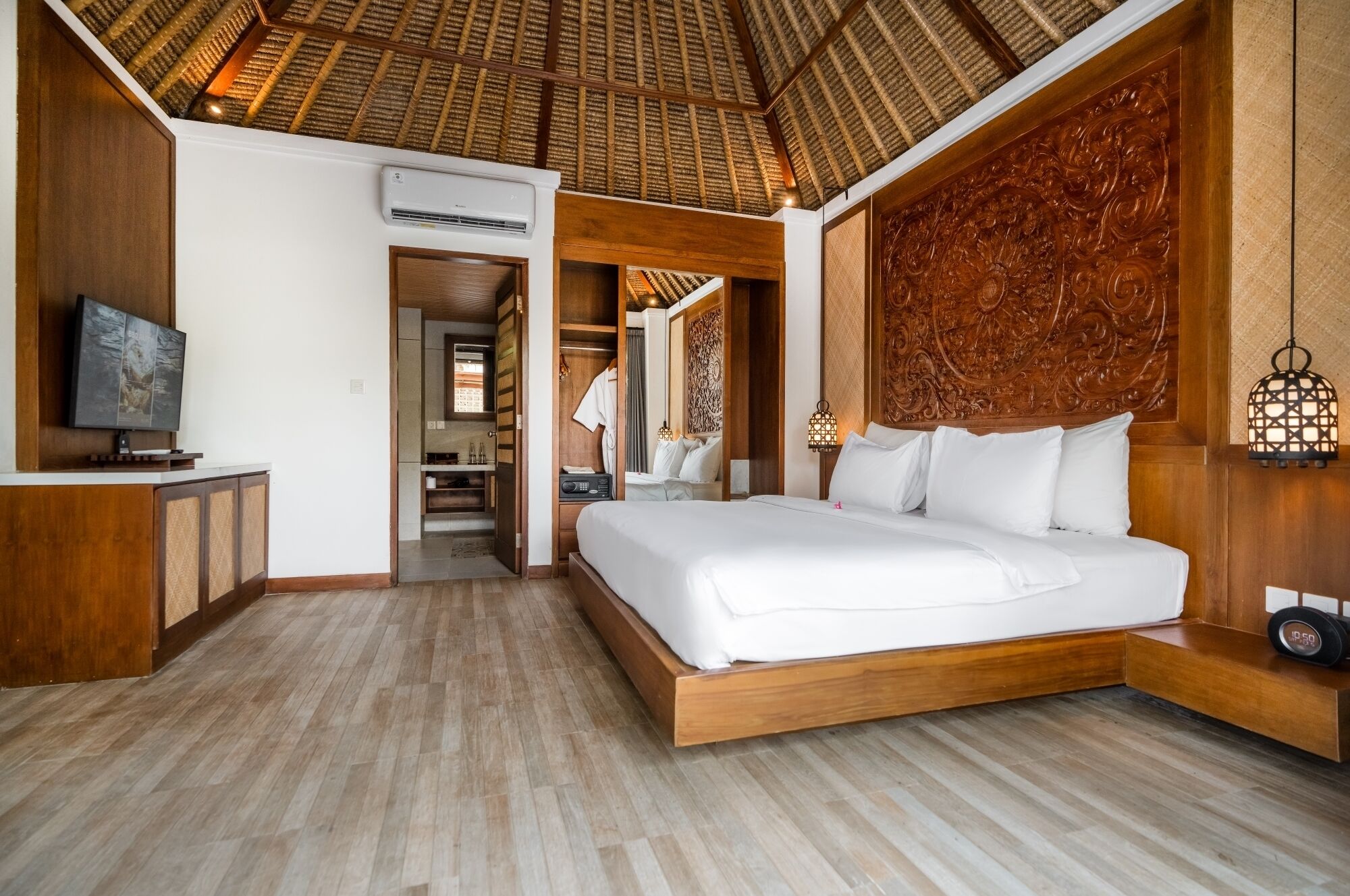 A modern hotel room with a large bed, wooden flooring, a TV, and a wardrobe.