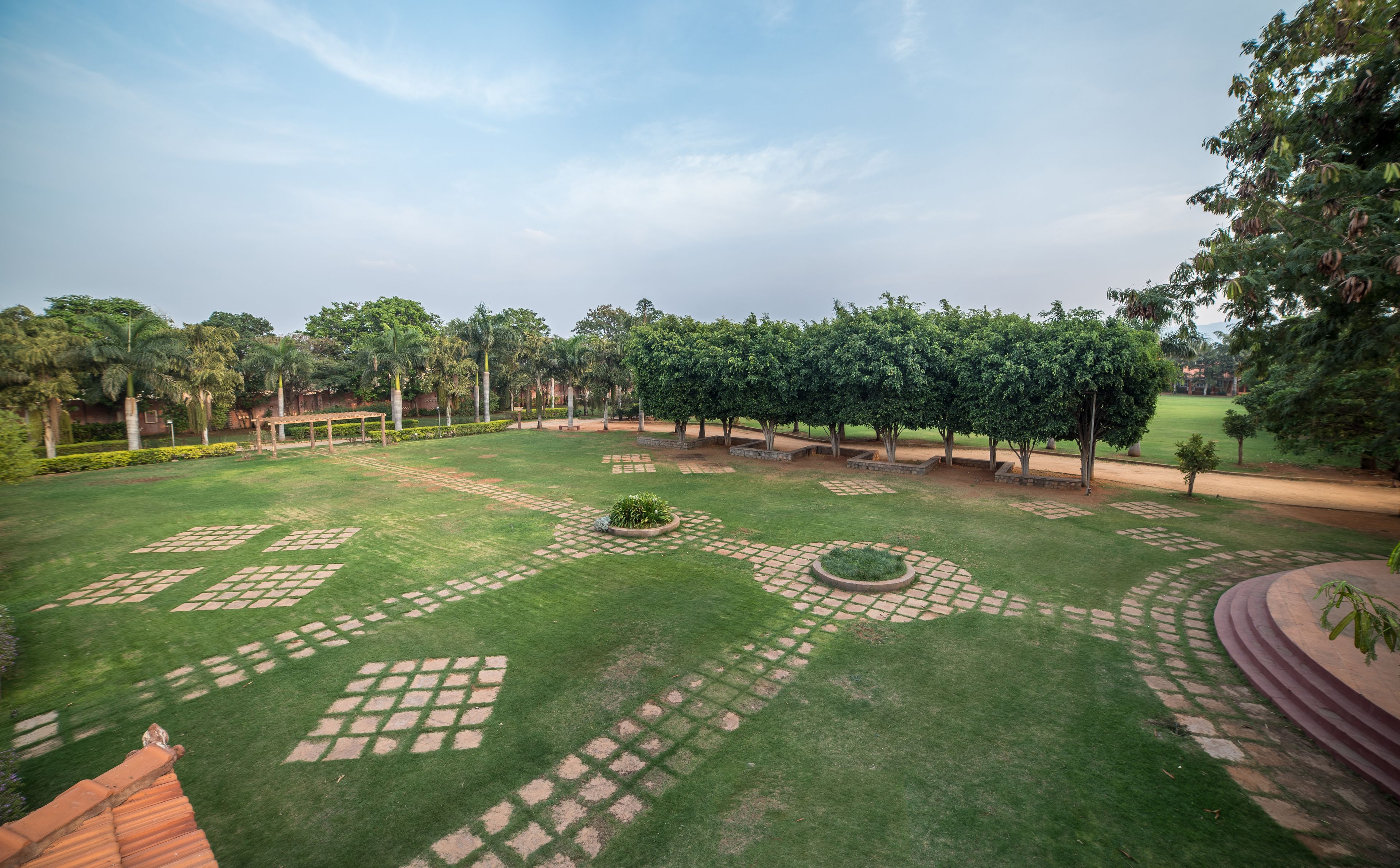 A well-maintained garden with a variety of trees, a central circular flower bed, and a paved walkway.