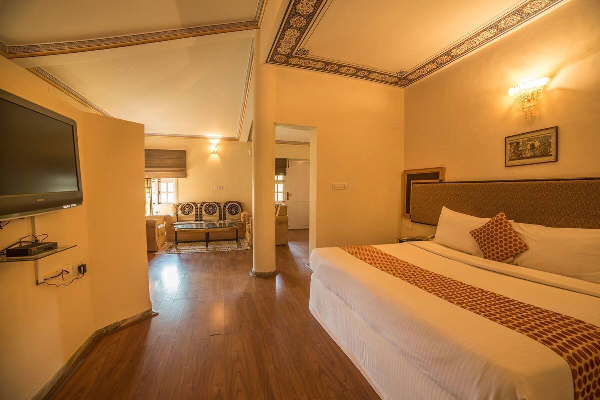 A hotel room with a bed, a TV, a dining area, and a hallway.