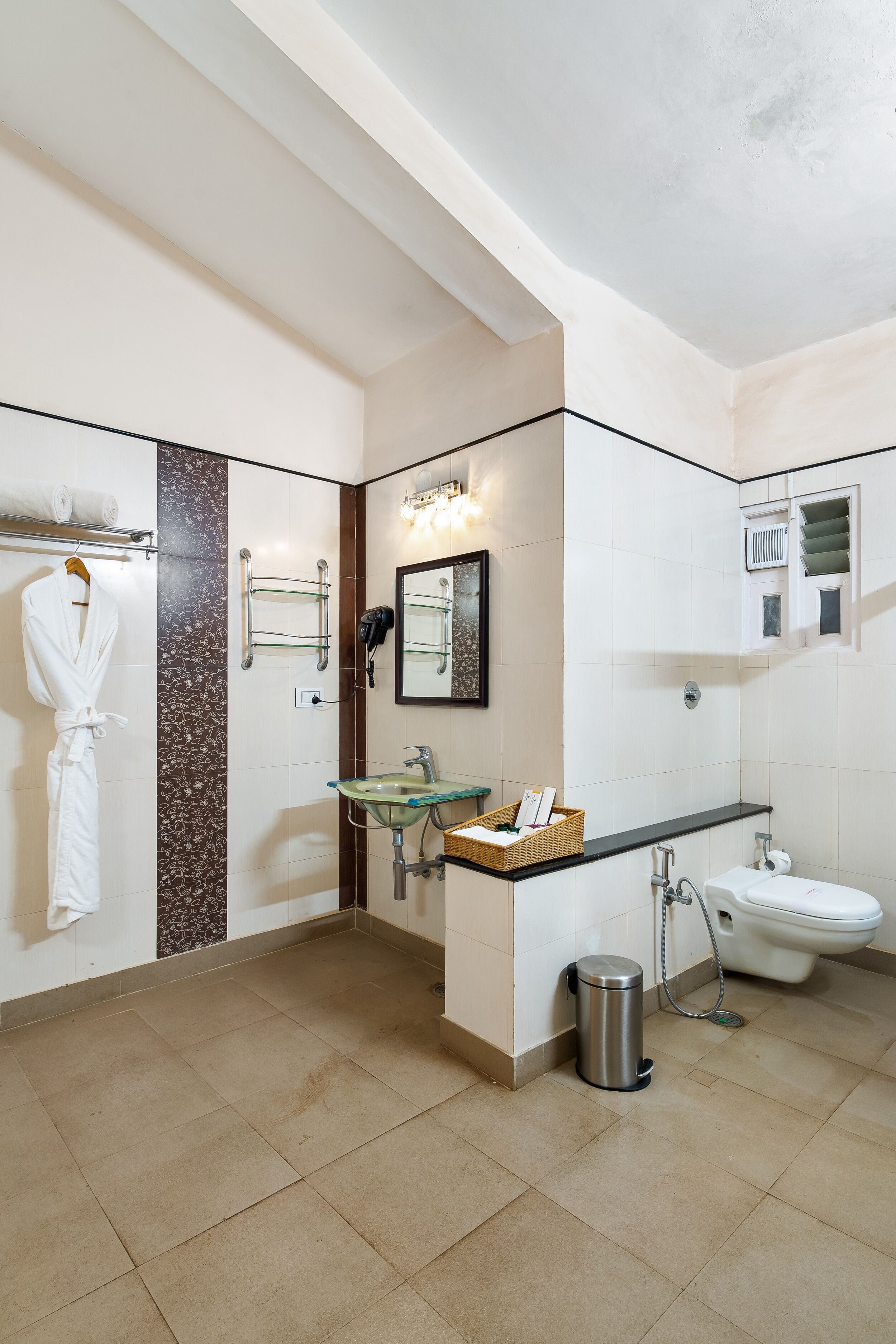 Un baño moderno con un lavamanos de vidrio, un inodoro blanco, una bata colgada en un perchero y un tozalete.