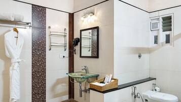 Un baño moderno con un lavamanos de vidrio, un inodoro blanco, una bata colgada en un perchero y un tozalete.