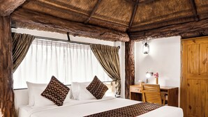 Techo de madera rústico, cama con ropa de cama blanca y almohadas estampadas, escritorio con silla y armario de madera.
