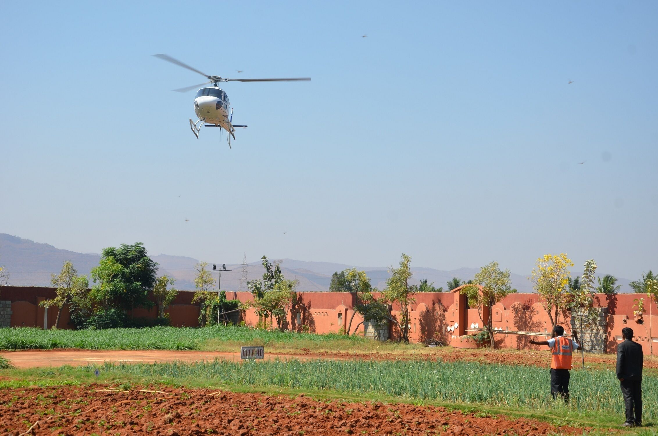 A helicopter flying over a rural landscape with buildings and fields.